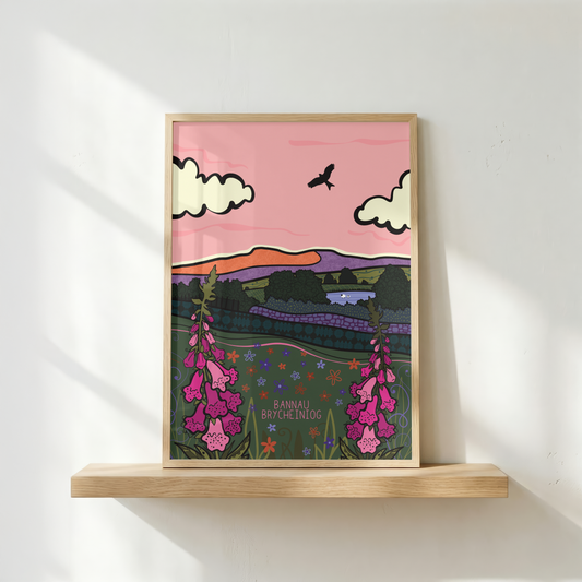 A framed art print featuring a stylized landscape illustration with pink sky, white clouds, a bird, purple hills, and pink foxglove flowers, displayed on a light wood floating shelf against a white wall with soft window shadows.